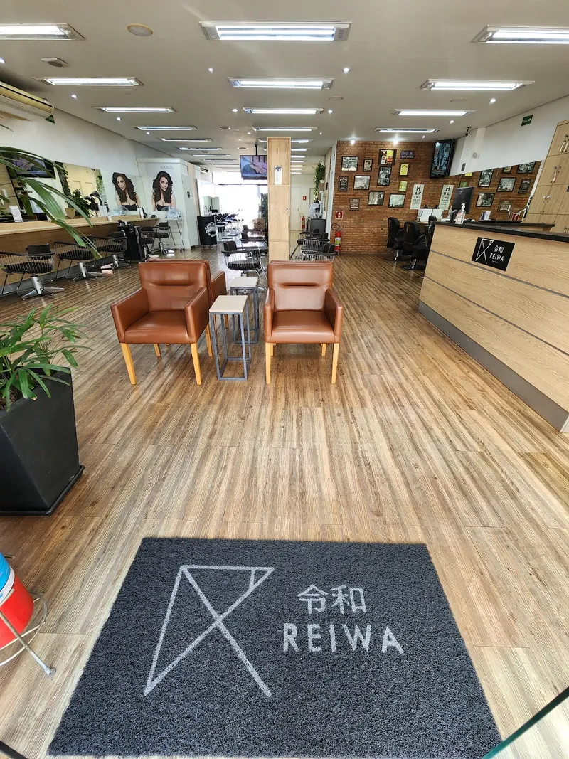 Entrada do Studio Reiwa com tapete preto com a marca Reiwa, poltronas de espera e salão ao fundo